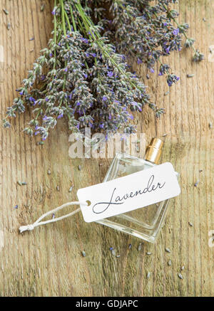 Parfum de lavande dans une bouteille avec des fleurs de lavande et de l'étiquette sur fond rustique en bois Banque D'Images