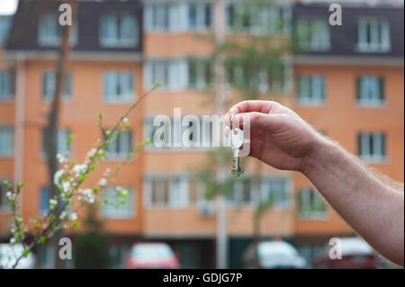 La main de l'homme détenant les clés de l'appartement sur l'arrière-plan d'un immeuble de plusieurs étages Banque D'Images