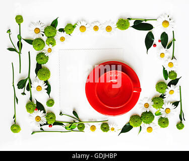 Tasse rouge et du papier pour le café ou le thé avec floral frame à partir de camomille et de fleurs de chrysanthème, ficus feuilles et ripe rowan sur w Banque D'Images