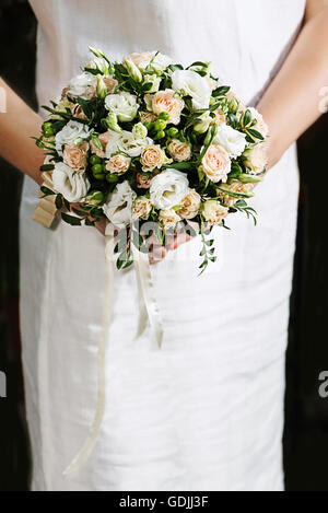 Suite nuptiale colorés beau bouquet de roses de différentes couleurs et d'autres fleurs dans les mains de la mariée en robe blanche. Banque D'Images