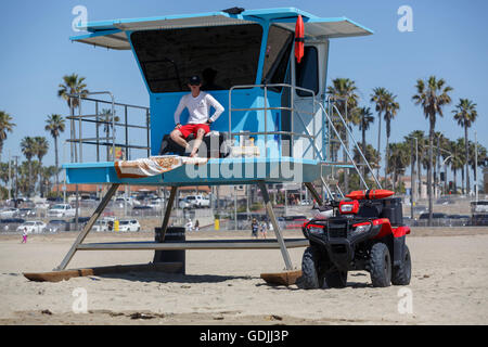 Peint bleu lifeguard poste numéro 4 avec Huntigton Beach lifeguard assis attentivement et sa Honda ATV garé ci-dessous Banque D'Images