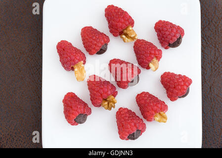 Les framboises rouges traite avec des noix, des pépites de chocolat et aménagé en rangées sur une plaque blanche Banque D'Images