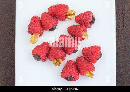 Les framboises rouges traite avec des noix, des pépites de chocolat et aménagé en rangées sur une plaque blanche Banque D'Images