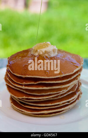 Des crêpes avec du beurre et du miel sur la plaque blanche dans le jardin ou sur la nature. Verser le sirop sur la pile de crêpes. Banque D'Images