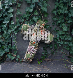 Croix faite de mousse et de fleurs séchées décorant une vieille pierre tombale avant Toussaint à Lodz, Pologne. Banque D'Images