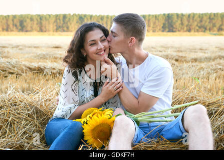 Happy young couple assis dans wheaten field au soir, romantique personnes concept, beau paysage, saison d'été Banque D'Images