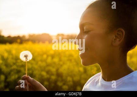 Beautiful happy mixed race African American girl adolescent femme jeune femme smiling in golden sunset light avec dandelion clock Banque D'Images