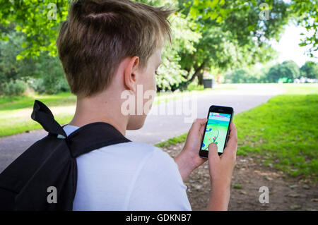 Un garçon dans le parc et jouent le nouveau Pokemon le jeu de Go sur son téléphone Banque D'Images