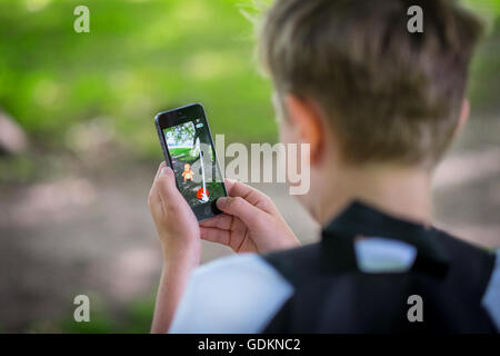 Un garçon dans le parc et jouent le nouveau Pokemon le jeu de Go sur son téléphone Banque D'Images