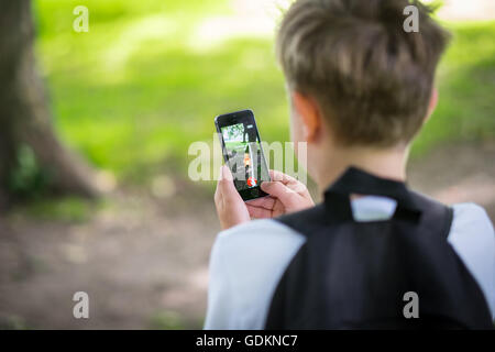 Un garçon dans le parc et jouent le nouveau Pokemon le jeu de Go sur son téléphone Banque D'Images