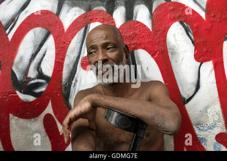 Adilson Rosa da Mata (51) se trouve en face d'un graffiti à lire 'Complexo do Alemão" à Rio de Janeiro, Brésil, 16.07.2016. Il a vécu dans la favela depuis 50 ans et souffre de diabète après plusieurs années dans l'industrie de transformation des métaux. L'argent d'incapacité de travail par le gouvernement s'élève à seulement 800 reais (environ 270 Euros) et n'est pas suffisante pour la survie. Il gagne un peu d'argent par la collecte de bouteilles vides. Photo : Peter Bauza/dpa Banque D'Images