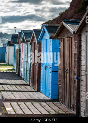 Scène de bord de mer représentant une rangée de cabines de plage multicolores, sentier à lattes, plage de galets et la côte jurassique. Banque D'Images
