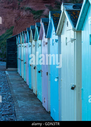 Scène de bord de mer représentant une rangée de cabines de plage multicolores, voie d'asphalte, plage de galets et la côte jurassique. Banque D'Images