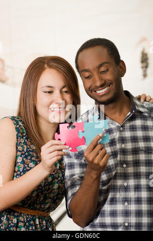 Charmant couple interracial friendly, holding de grandes pièces de puzzle et heureusement l'interaction s'amusant, floue fond studio Banque D'Images