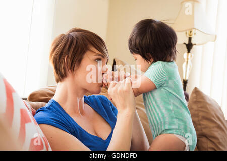 Mother sitting on sofa kissing baby's hands Banque D'Images