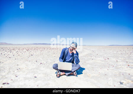 Man sitting cross legged dans désert recherche sur ordinateur portable, Nevada, USA Banque D'Images