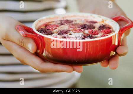 Woman holding fresh Cherry clafoutis dans un ramequin rouge Banque D'Images
