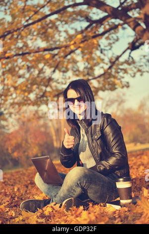 Woman in park with laptop showing thumb up Banque D'Images