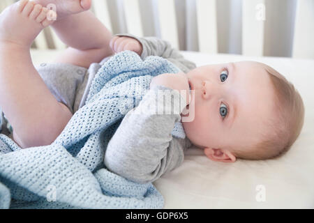 Portrait de blue eyed baby boy lying in crib avec comfort blanket Banque D'Images