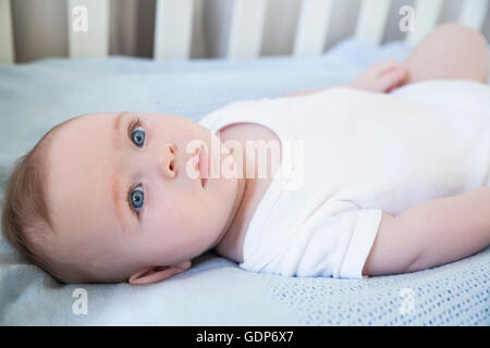 Blue Eyed baby garçon couché dans son lit de bébé Banque D'Images