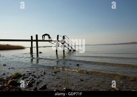 Silhouette of woman on pier bending over backwards in yoga position Banque D'Images