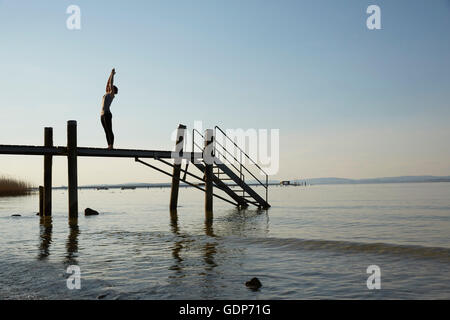 Silhouette of woman on pier bras levés in yoga position Banque D'Images