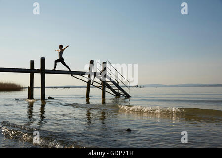 Silhouette de femme sur la jetée les bras ouverts, les jambes en position de yoga Banque D'Images