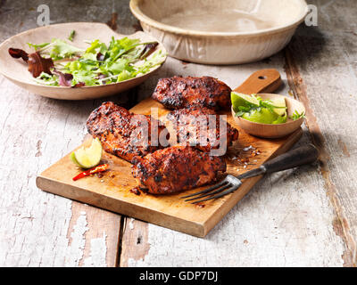 La nourriture, Deli poulets cuisses Caroline, planche à découper en bois, citron vert frais et le piment, salade au bol en bois, table en bois rustique Banque D'Images