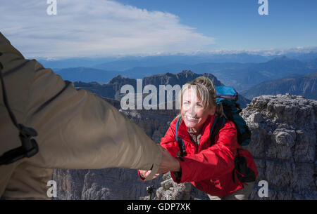 Un grimpeur mâle aider sa partenaire féminine pour atteindre le sommet d'une montagne, Dolomites, Italie Banque D'Images