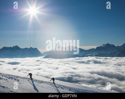 Deux alpinistes sur une pente enneigée au-dessus d'une mer de brume dans une vallée alpine, Alpes, Canton du Valais, Suisse Banque D'Images