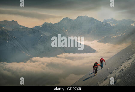 Deux alpinistes sur une pente enneigée sur une mer de brume dans une vallée alpine, Alpes, Canton du Valais, Suisse Banque D'Images