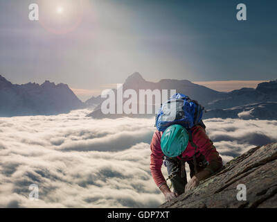 Grimpeur sur un mur rocheux au-dessus d'une mer de brume dans une vallée alpine, Alpes, Canton du Valais, Suisse Banque D'Images