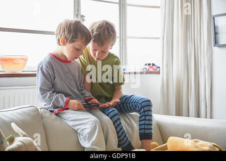 Garçons en pyjama sitting on sofa looking at smartphone Banque D'Images