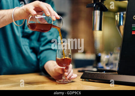 Mains d'homme froid préparer de café barista pouring into wine glass sur le café au comptoir Banque D'Images