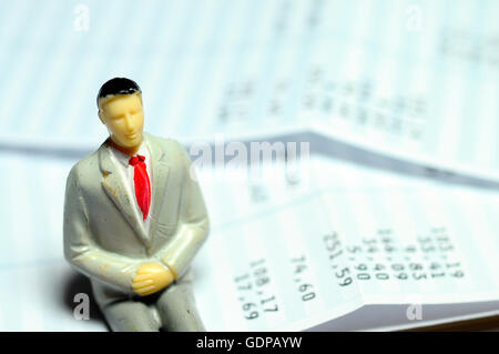 Businessman figure miniature assis sur sa masse salariale Banque D'Images