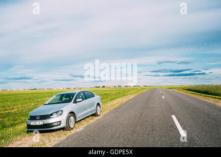 Gomel, Bélarus - 13 juin, 2016 : Volkswagen Polo Parking voiture sur l'accotement des routes de campagne, sur fond de champs de printemps vert Banque D'Images