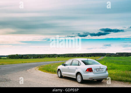 Gomel, Bélarus - 13 juin, 2016 : Volkswagen Polo Parking voiture sur l'accotement des routes de campagne, sur fond de champs de printemps vert Banque D'Images