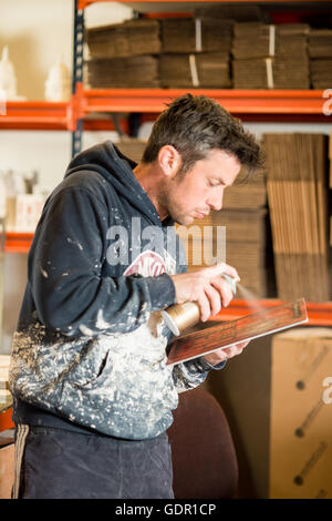 Homme debout en train de peindre une petite planche en bois à l'aide de peinture en aérosol Banque D'Images