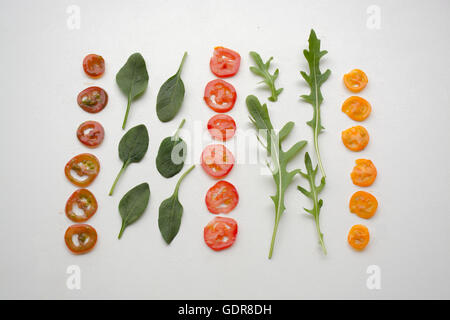 Trois types de tranches de tomates cerises avec bébés épinards et roquette (aragula) feuilles formant une salade déconstruit Banque D'Images