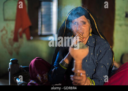 Barsana, Inde - 28 Février 2015 : les femmes rurales indiennes portant des vêtements traditionnels assis sur lit bébé fumer le narguilé pipe. Banque D'Images