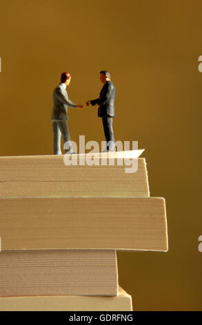 Univers miniatures shaking hands on pile of books Banque D'Images