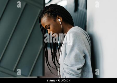 Demi-longueur close-up portrait of young girl wearing excité hoodie et écouteurs cool looking down permanent Banque D'Images