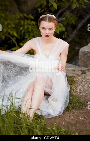 Jeune fille dans une robe en dentelle blanche style Boho ajuste son aux genoux. Assis sur les rochers Banque D'Images