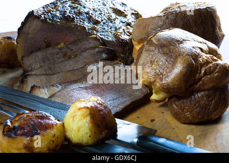 Un petit-déjeuner anglais fraîchement rôti de boeuf partiellement sculptés sur une planche en bois avec quelques pommes de terre, prêt à servir. Banque D'Images