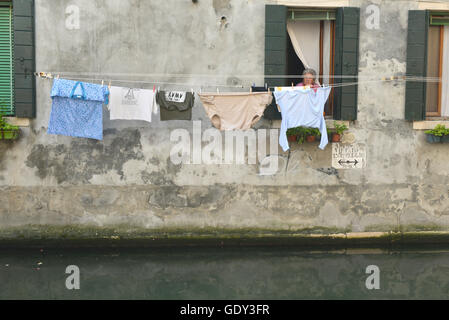 Une femme étendre le linge sur une ligne sur un canal à Venise, Italie Banque D'Images