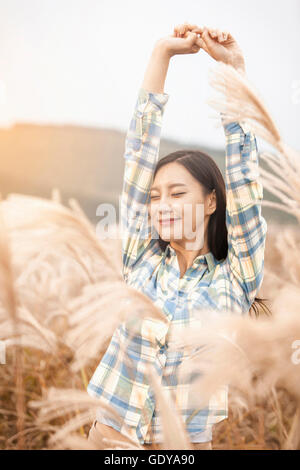 Portrait of young smiling woman stretching her arms fermant les yeux dans l'herbe d'argent Banque D'Images