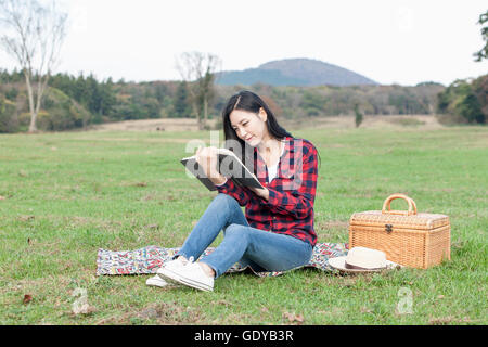 Jeune femme assis sur les herbages et la lecture d'un livre lors de pique-nique Banque D'Images