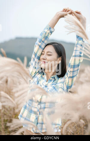 Portrait of young smiling woman stretching her arms fermer les yeux en argent grass field Banque D'Images