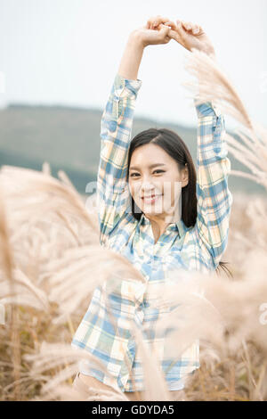 Portrait of young smiling woman stretching her arms à silver grass field Banque D'Images