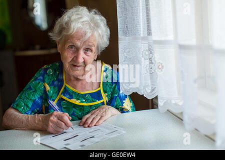 Femme à la retraite remplit les factures de services à la maison derrière une table. Banque D'Images